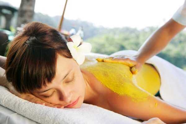 Mujer acostada boca abajo en camilla de masaje mientras recibe un masaje de espalda con polvos de mostaza.