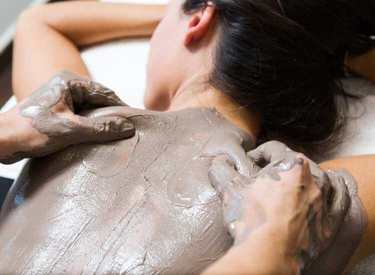 Masajista realizando masaje estético y relajante en la espalda de una mujer, aplicando una mascarilla de lodo.