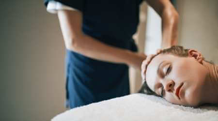 Mujer acostada en camilla recibiendo un masaje relajante manual en la coronilla.