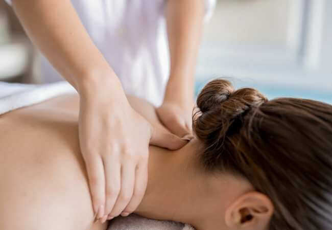 Mujer acostada boca abajo mientras recibe un masaje en la nuca, cuello y hombros para aliviar el dolor de los nervios y columna.