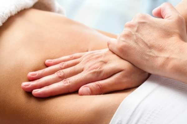 Terapeuta realizando presiones y movilizaciones con la palma de su mano sobre el vientre de su clienta, a modo de drenar y reequilibrar el sistema digestivo